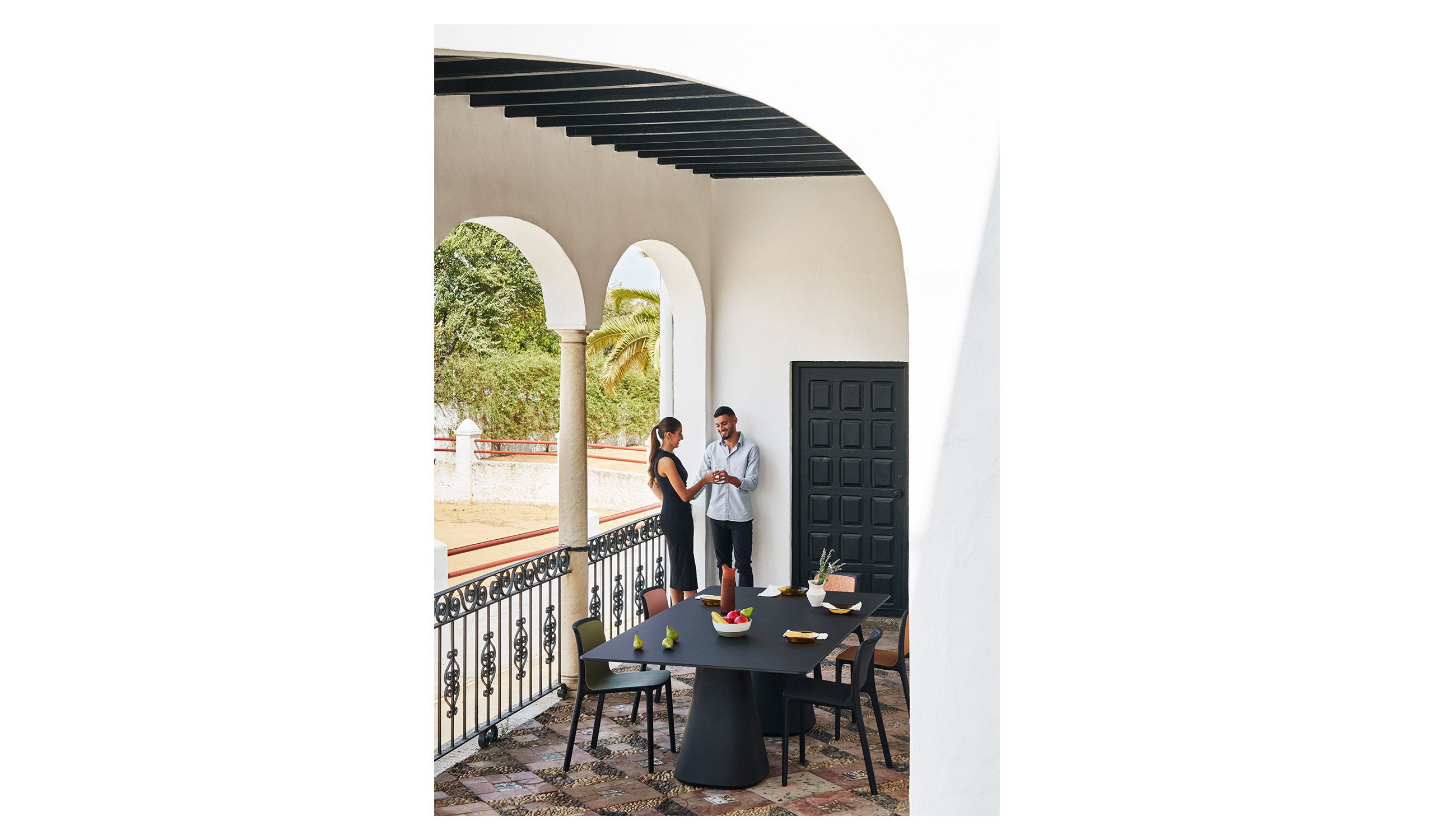 Terraza con arcos y columnas de inspiración andaluza. Escena con mobiliario de diseño contemporáneo y dos personas de sobremesa